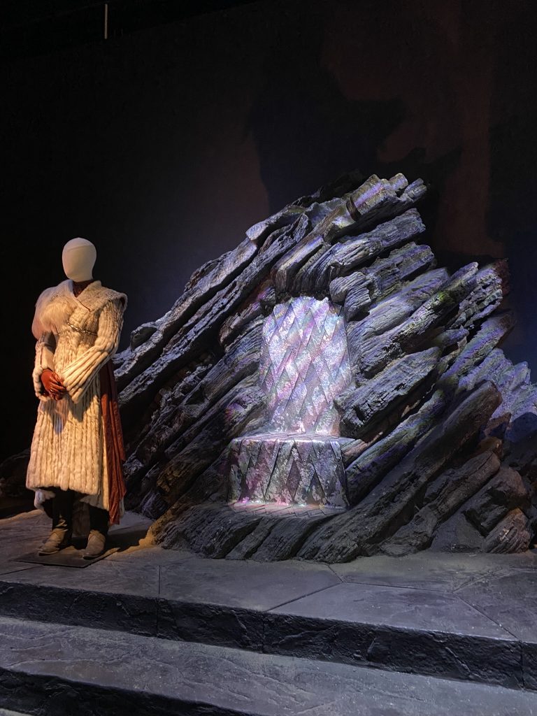 Statue de Daenerys Targaryen debout à côté du trône de Peyredragon aux studios Game of Thrones, ambiance sombre et décor fidèle à la série